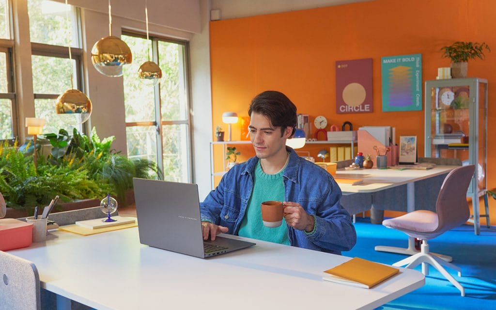 Seorang pria sedang menggunakan Laptop AI 2025 ASUS Vivobook S14 sambil menikmati kopi di kafe, menunjukkan fleksibilitas dan gaya hidup modern.