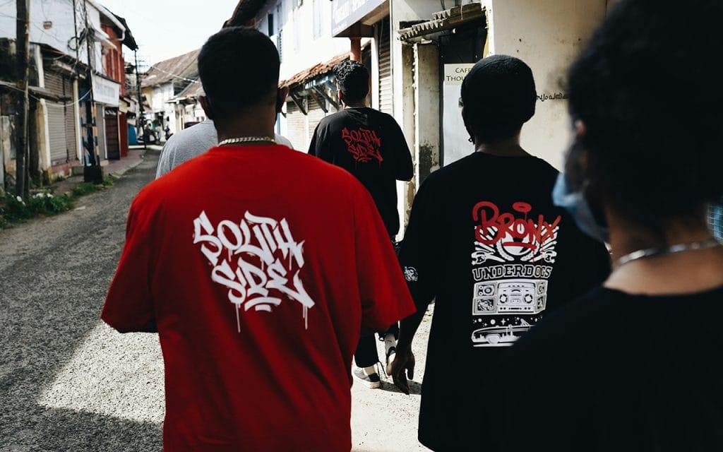 Sekelompok anak muda mengenakan kaos oversized dengan desain tagging graffiti, mencerminkan ciri khas gaya streetwear urban