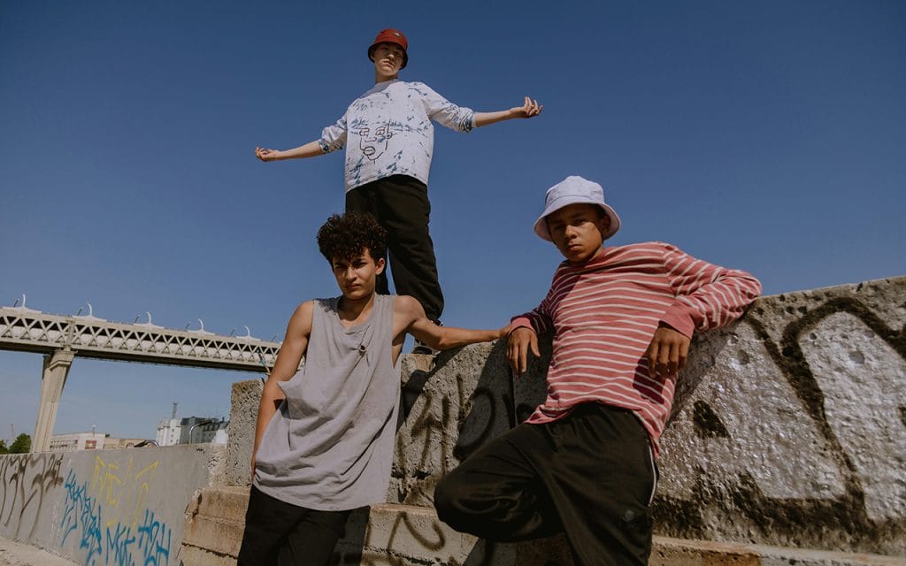 Remaja laki-laki bergaya streetwear kasual mengenakan bucket hat bersandar di dinding graffiti