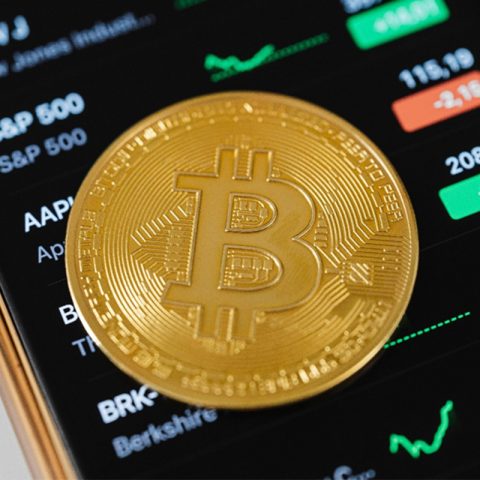 Bitcoin dengan latar belakang grafik harga kripto sebagai ilustrasi investasi crypto untuk pemula