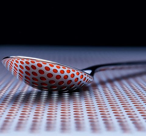 Sendok logam dengan pola titik merah yang dipantulkan pada permukaan berlubang dalam konsep Abstract Photography.