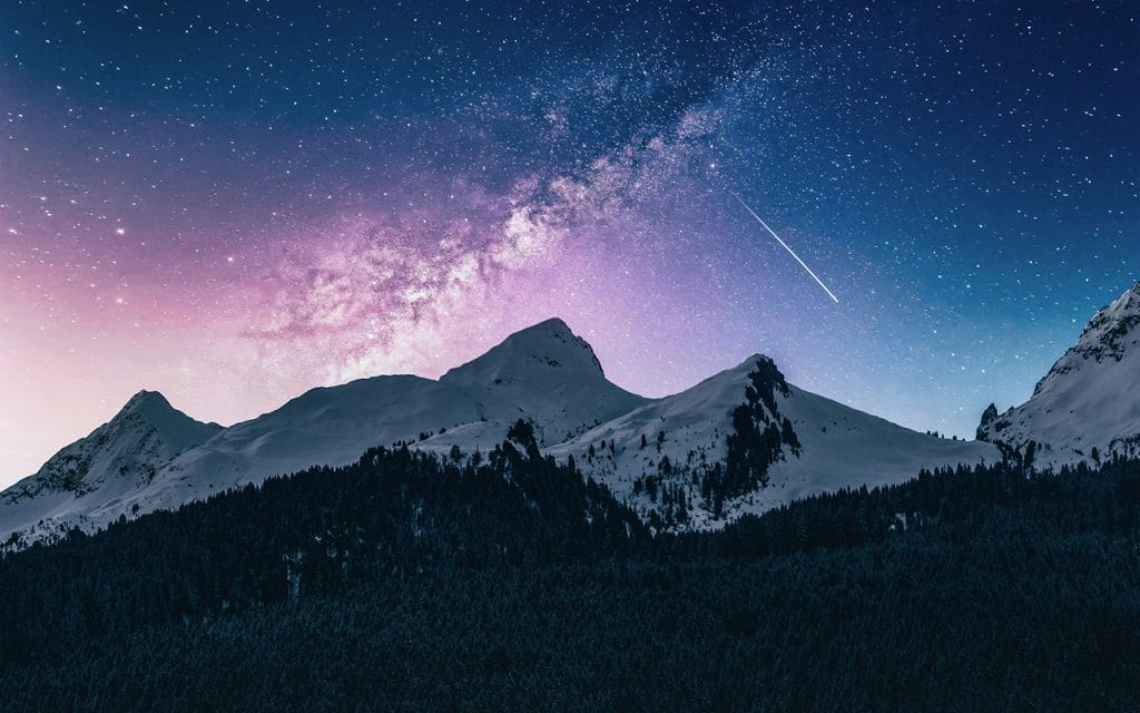 Foto Astrophotography menampilkan galaksi Bima Sakti di langit malam berbintang di atas pegunungan bersalju dengan jejak meteor, menggambarkan keindahan alam semesta dalam suasana tenang dan megah