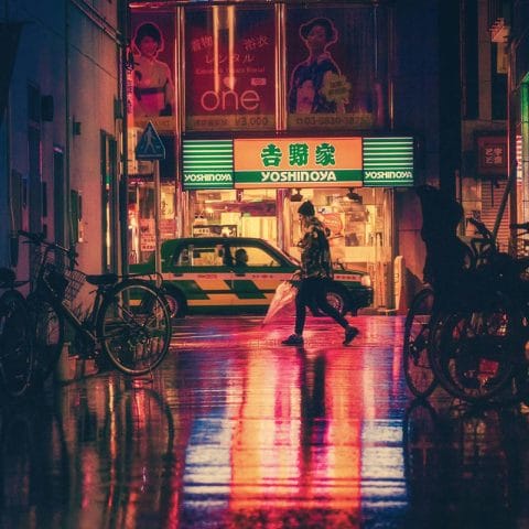Pejalan kaki menyeberang di jalan kota dengan cahaya neon pada malam hari, contoh foto urban photography