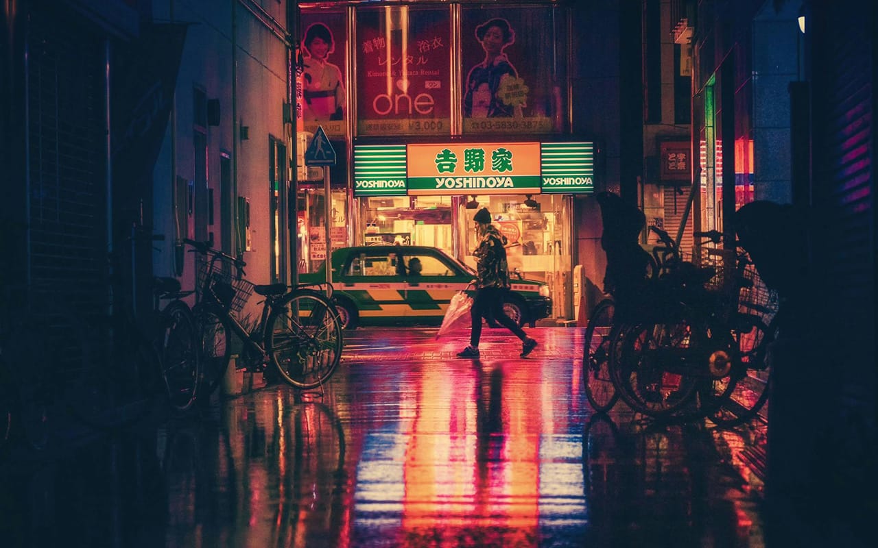 Pejalan kaki menyeberang di jalan kota dengan cahaya neon pada malam hari, contoh foto urban photography