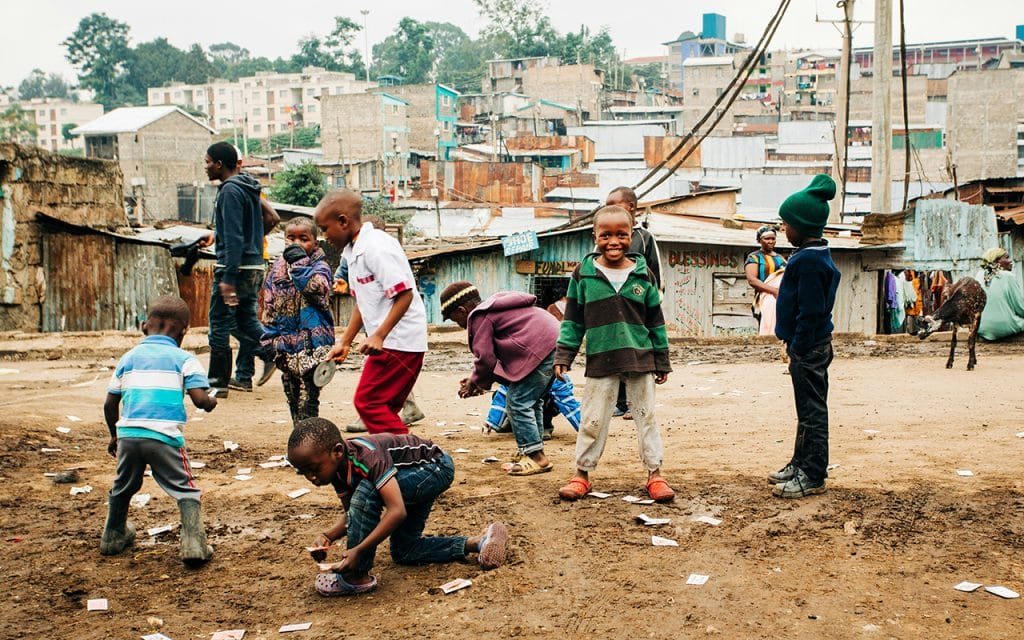 Fotografi dokumenter anak-anak bermain di lingkungan padat penduduk dengan latar perumahan sederhana