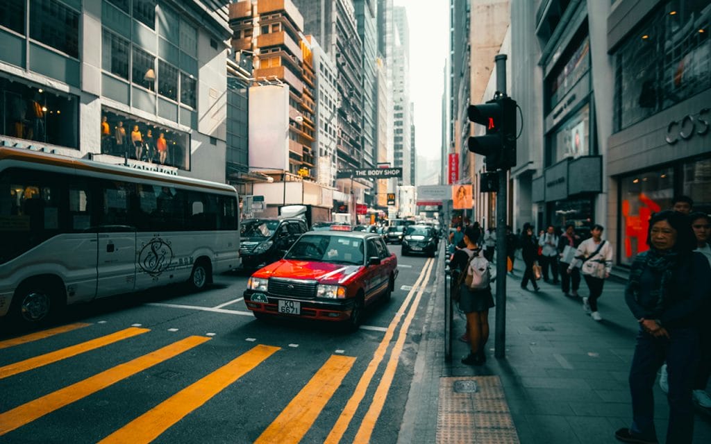 Foto suasana jalanan kota dengan mobil, bus, dan pejalan kaki, contoh fotografi jalanan yang menangkap kehidupan urban sehari-hari