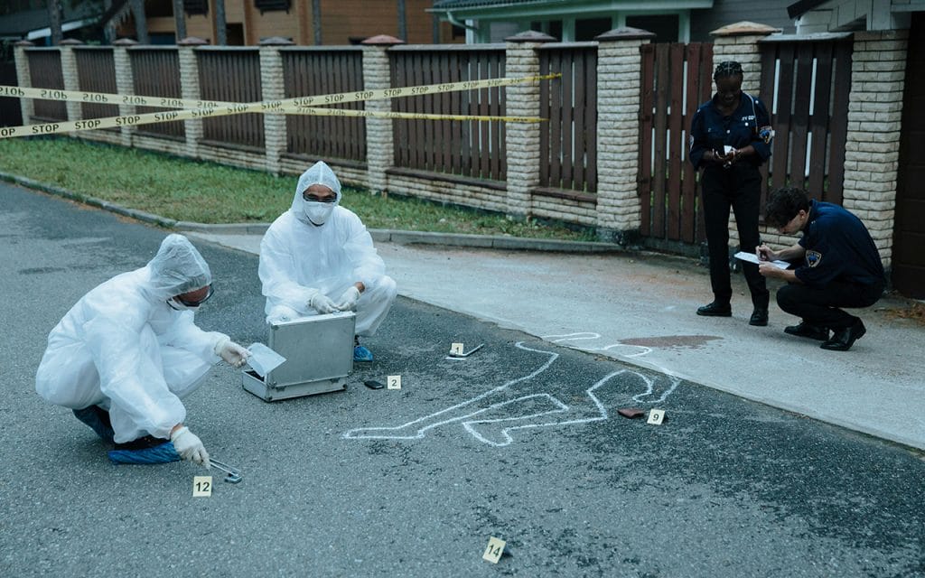 Tim forensik mengenakan pakaian pelindung sedang memeriksa dan mendokumentasikan barang bukti di tempat kejadian perkara dengan garis polisi di latar belakang