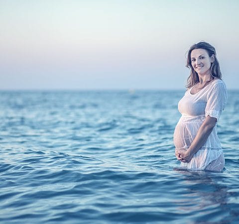 Ibu hamil tersenyum sambil memegang perut saat sesi maternity photography