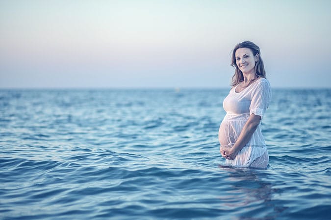 Ibu hamil tersenyum sambil memegang perut saat sesi maternity photography