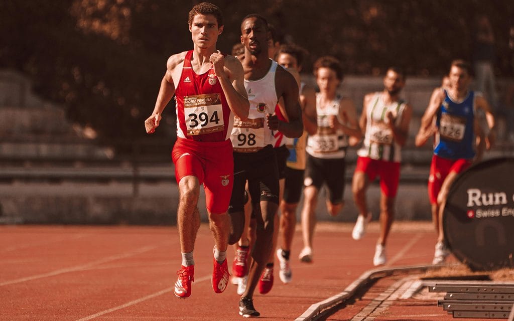 Seorang pelari memimpin lomba lari di lintasan atletik dengan beberapa peserta lain di belakangnya, menggambarkan momentum dramatis dalam sports photography