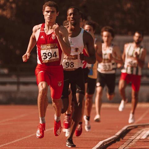 Seorang pelari memimpin lomba lari di lintasan atletik dengan beberapa peserta lain di belakangnya, menggambarkan momentum dramatis dalam sports photography