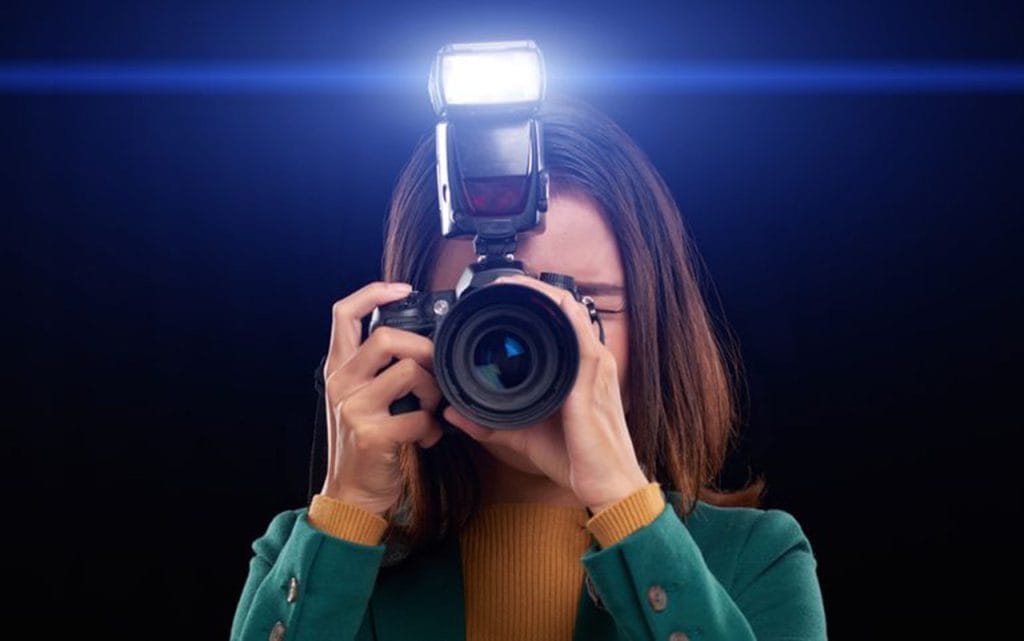 Fotografer wanita menggunakan kamera dengan flash eksternal menyala saat memotret di studio