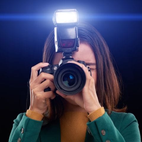 Fotografer wanita menggunakan kamera dengan flash eksternal menyala saat memotret di studio