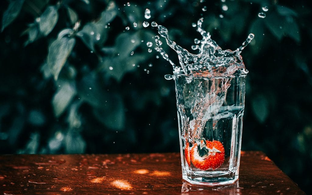 Contoh foto teknik freezing movement dengan shutter speed tinggi, menangkap percikan air dan stroberi yang jatuh ke dalam gelas