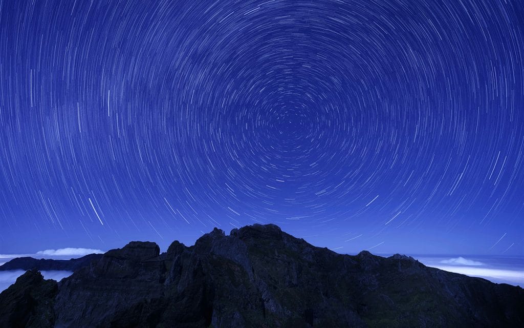 Contoh fotografi star trail yang menangkap jejak putaran bintang di langit malam menggunakan shutter speed sangat lama di area pegunungan