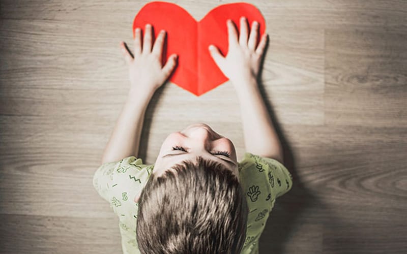 Foto anak memegang kertas berbentuk hati diambil dari sudut atas, contoh teknik high angle dalam fotografi