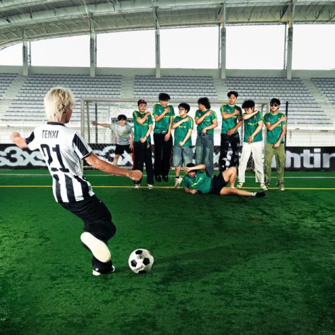 Cover album Liga Besar karya Tenxi menampilkan suasana stadion sepak bola dengan Tenxi bersiap menendang bola ke arah sekelompok pemain.